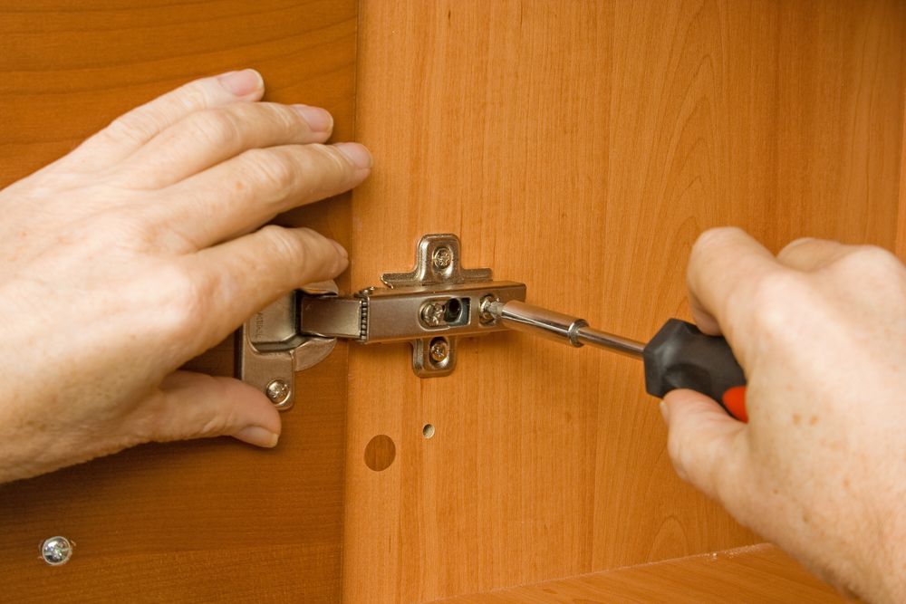 Person Installing a Cabinet Hinge With a Screwdriver on a Wooden Cabinet — Busy Bees Blasting in Trinity Beach, QLD
