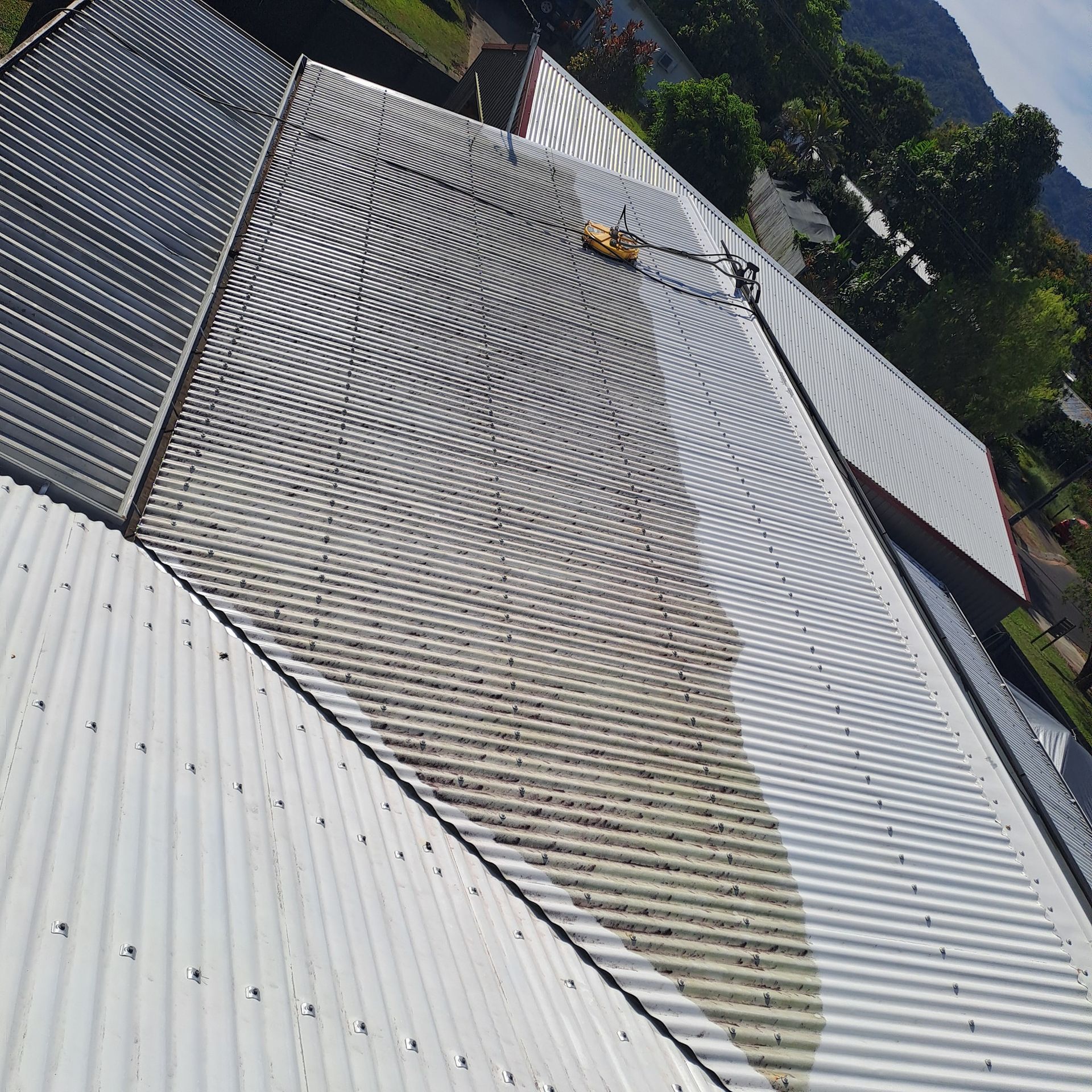 Metal Roof Being Cleaned; Pressure Washer Visible, Streaks of Dirt Show Contrast — Busy Bees Blasting in Trinity Beach, QLD