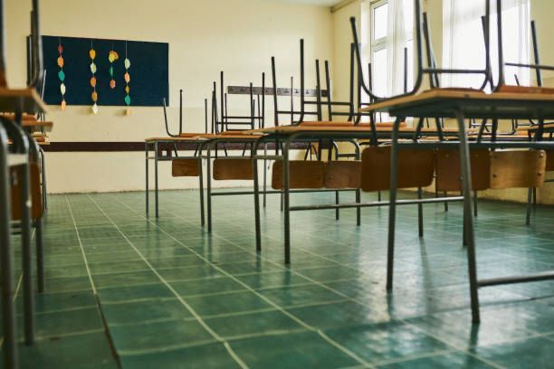 Ein leeres Klassenzimmer mit übereinander gestapelten Tischen und Stühlen.
