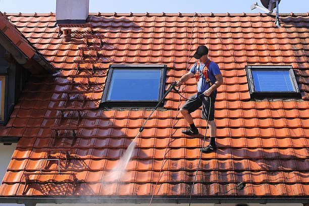 Ein Mann reinigt das Dach eines Hauses mit einem Hochdruckreiniger.