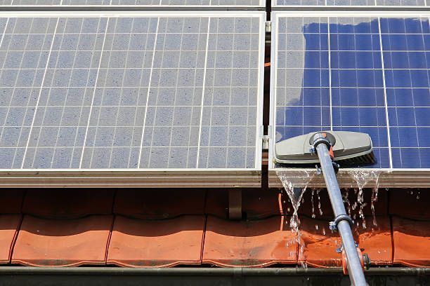 Eine Person reinigt Solarmodule auf einem Dach mit einer Bürste.