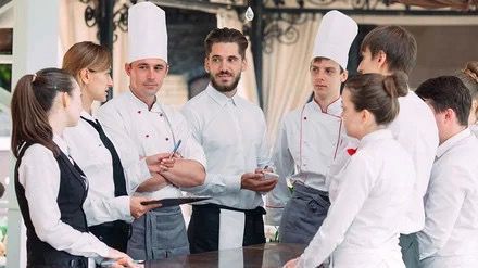 Eine Gruppe von Köchen und Kellnern steht in einem Restaurant um einen Tisch herum.