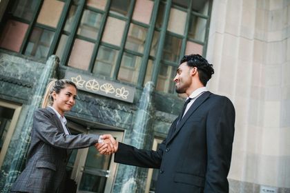 Ein Mann und eine Frau geben sich vor einem Gebäude die Hand.