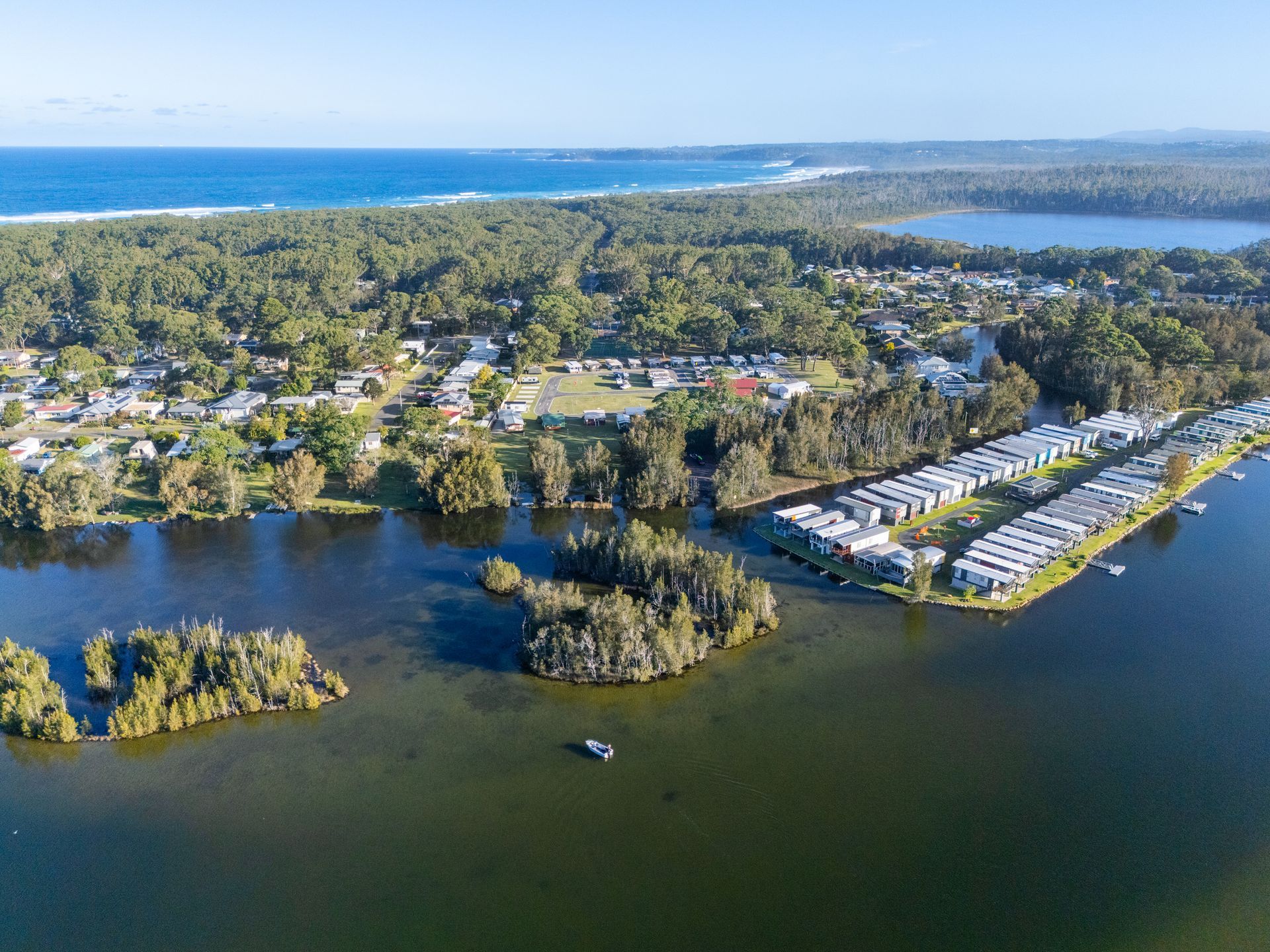 Aerial view: Lake with islands, town, forest, and ocean — SeaChange Parks Milton in Milton, NSW