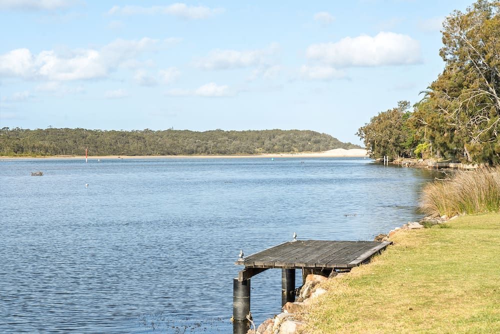 A Small Wooden Dock Extends Into a Calm River, Bordered — SeaChange Parks Milton in Milton, NSW