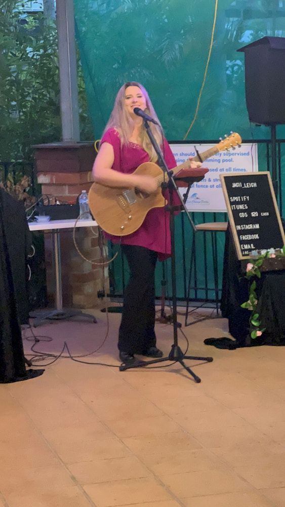 Woman With Guitar Sings Into Microphone Outdoors — SeaChange Parks Milton in Milton, NSW