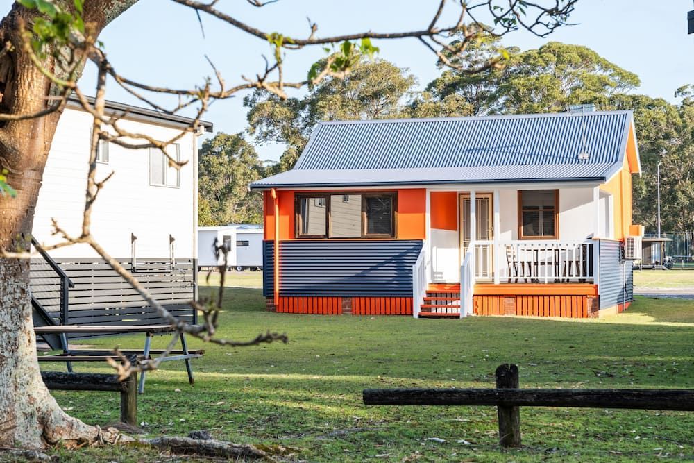 Colourful Cabin with Orange and Blue Accents, White Trim, and A Small Porch — SeaChange Parks Milton in Lake Conjola, NSW
