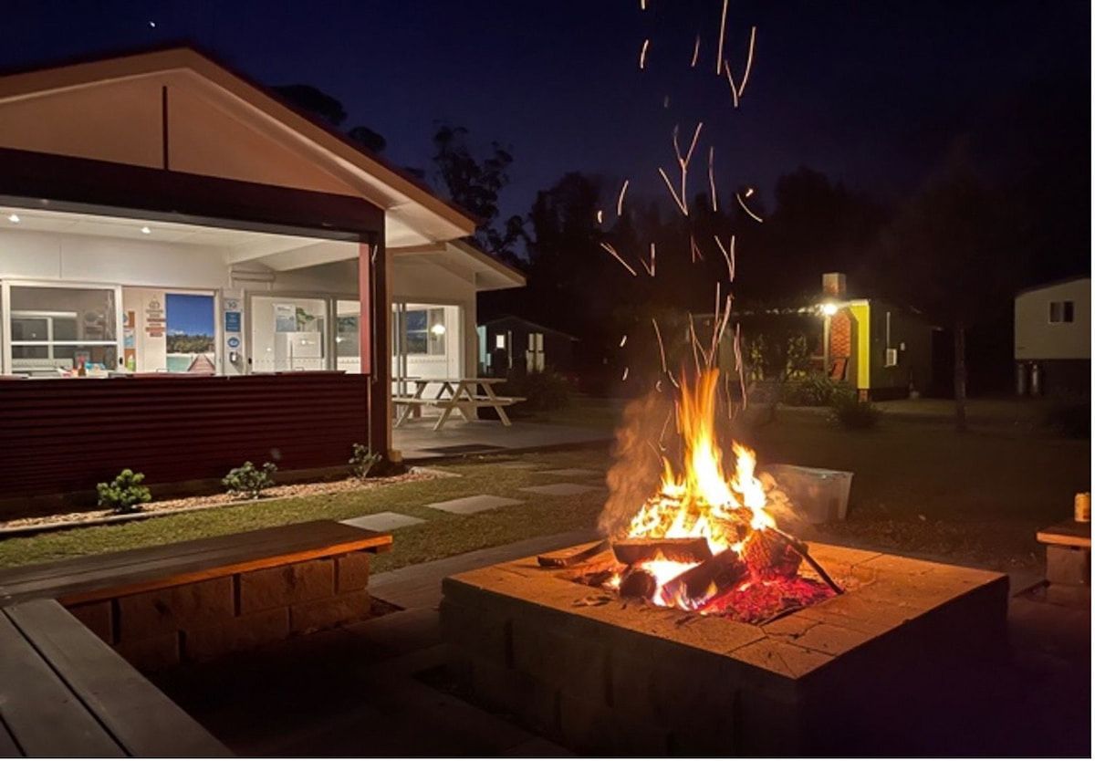 Backyard Fire Pit Glowing at Night Beside a Lit House and Outdoor Seating Area — SeaChange Parks Milton in Milton, NSW