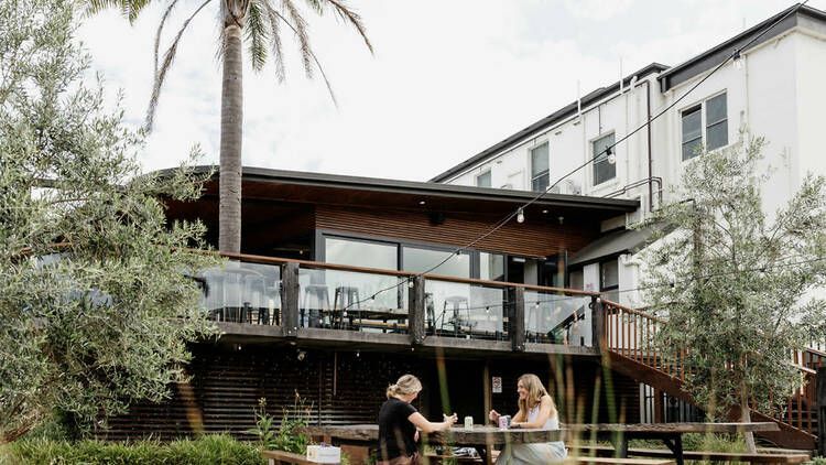 Two People Sit at an Outdoor Picnic Table on the Wooden Deck of a Modern Building— SeaChange Parks Milton in Milton, NSW