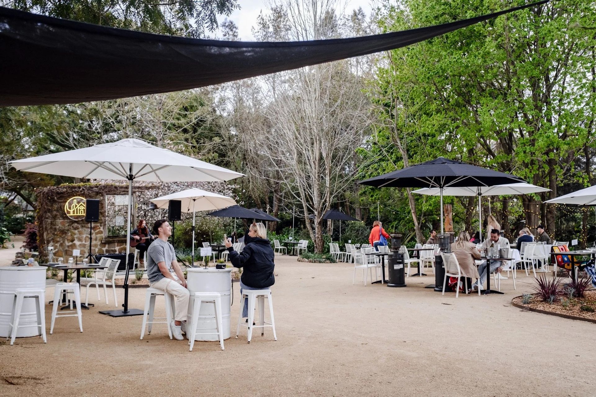 Patrons Sit at Outdoor Tables With Umbrellas in a Gravel Garden Café — SeaChange Parks Milton in Milton, NSW