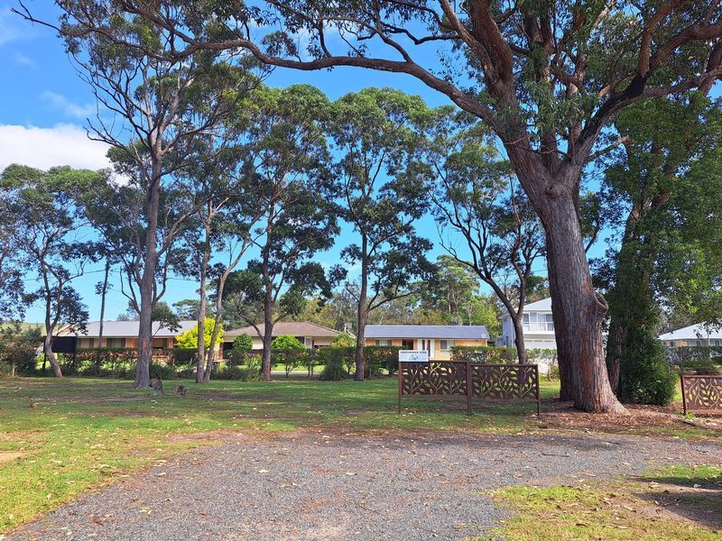 A Grassy Clearing with Trees, Gravel Foreground and Decorative Metal Benches — SeaChange Parks Milton in Lake Conjola, NSW
