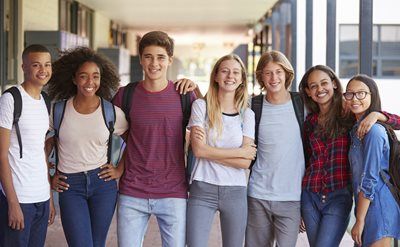 Group of smiling students in a school hallway, with backpacks.