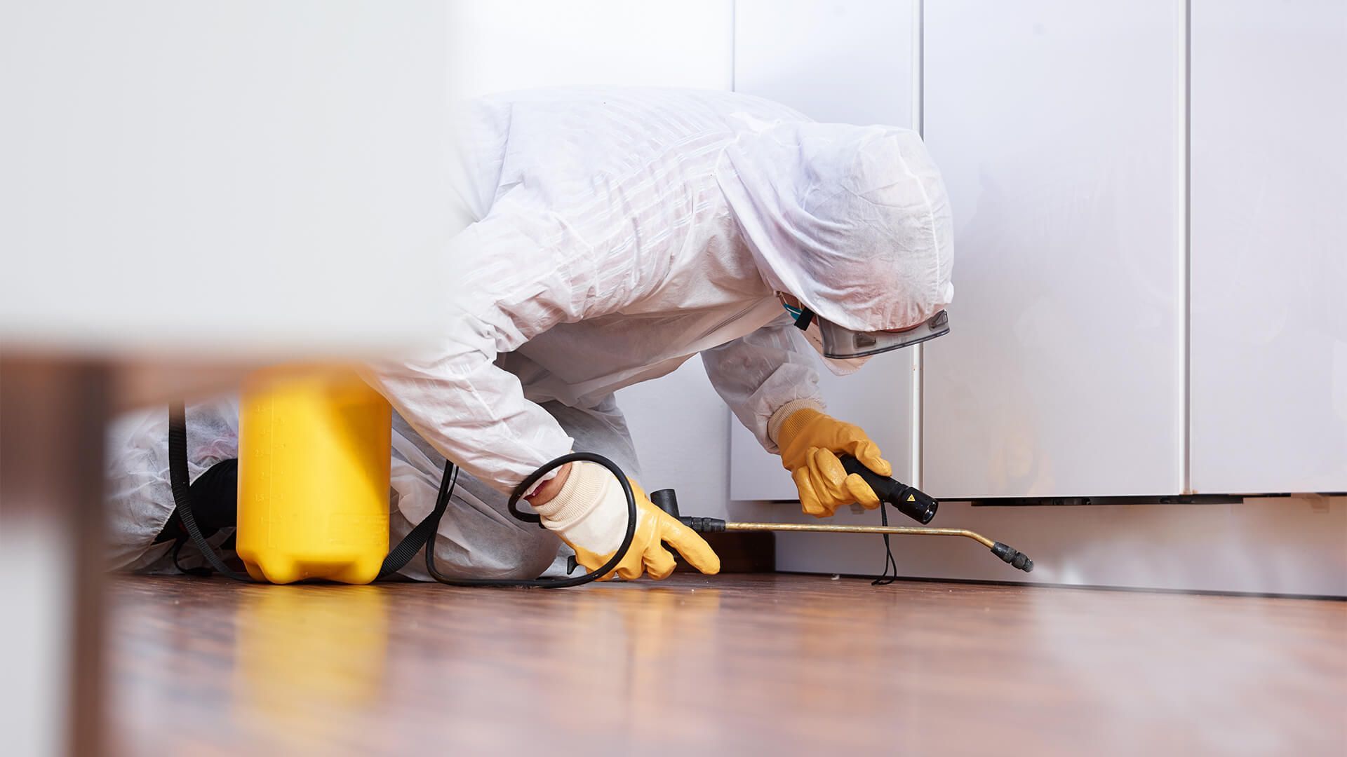 A man in a protective suit is spraying a room with a sprayer.