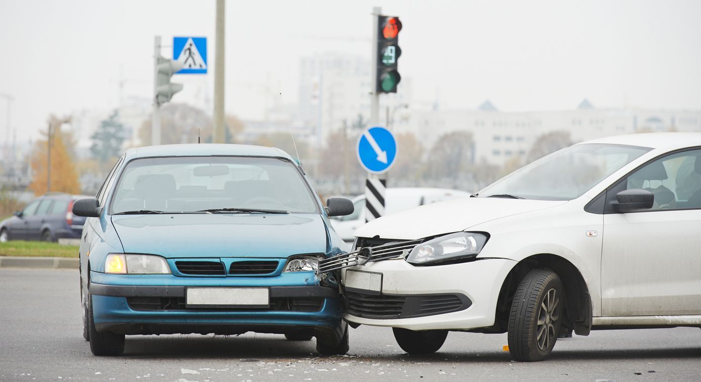 Two cars damaged in a collision at an intersection; one teal, one white.