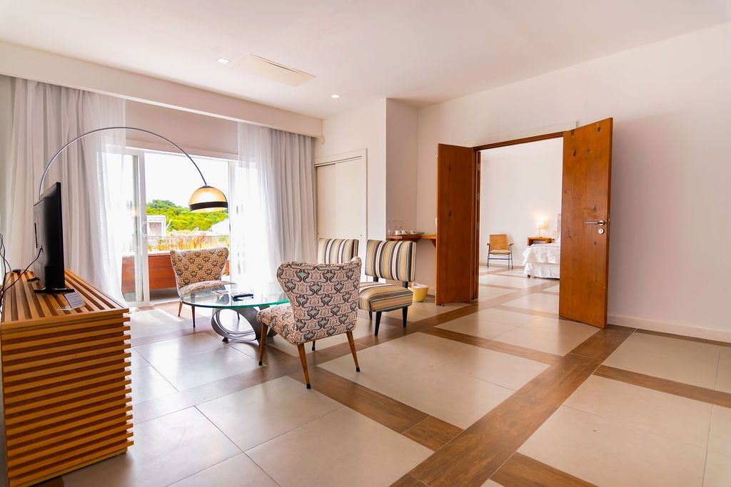 Sala de estar con puertas abiertas, piso de baldosas estampadas, acceso al balcón y varias sillas.