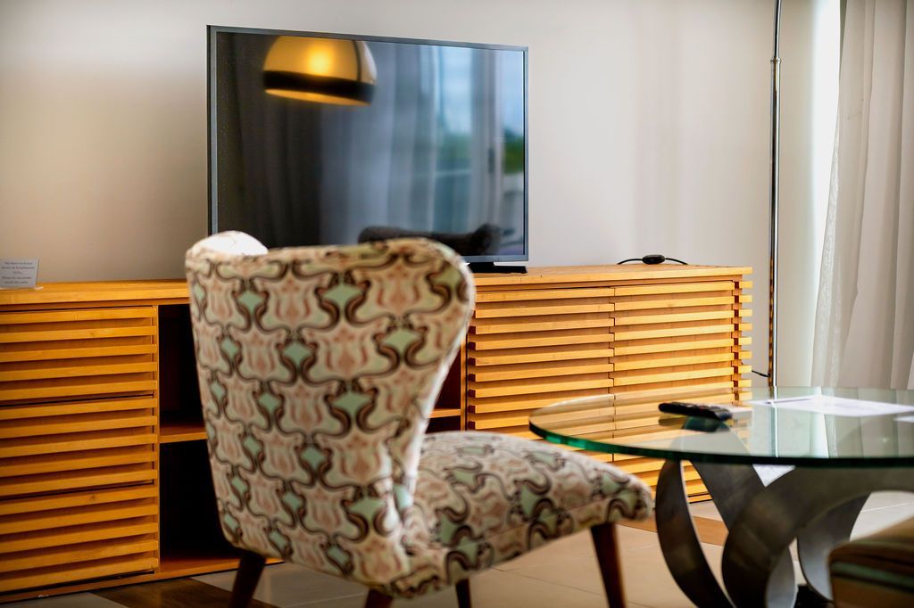 Sala de estar con silla estampada, TV, mueble de madera, mesa de cristal y lámpara colgante.