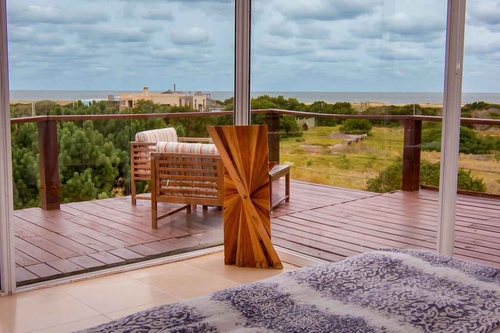 Terraza con asientos con vista al océano y dunas; cielo nublado.