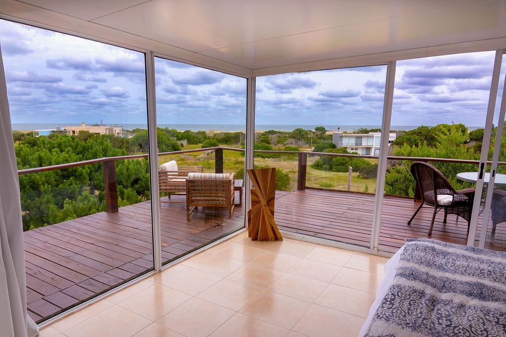 Una habitación luminosa con vista al mar a través de paredes de cristal y un deck de madera.