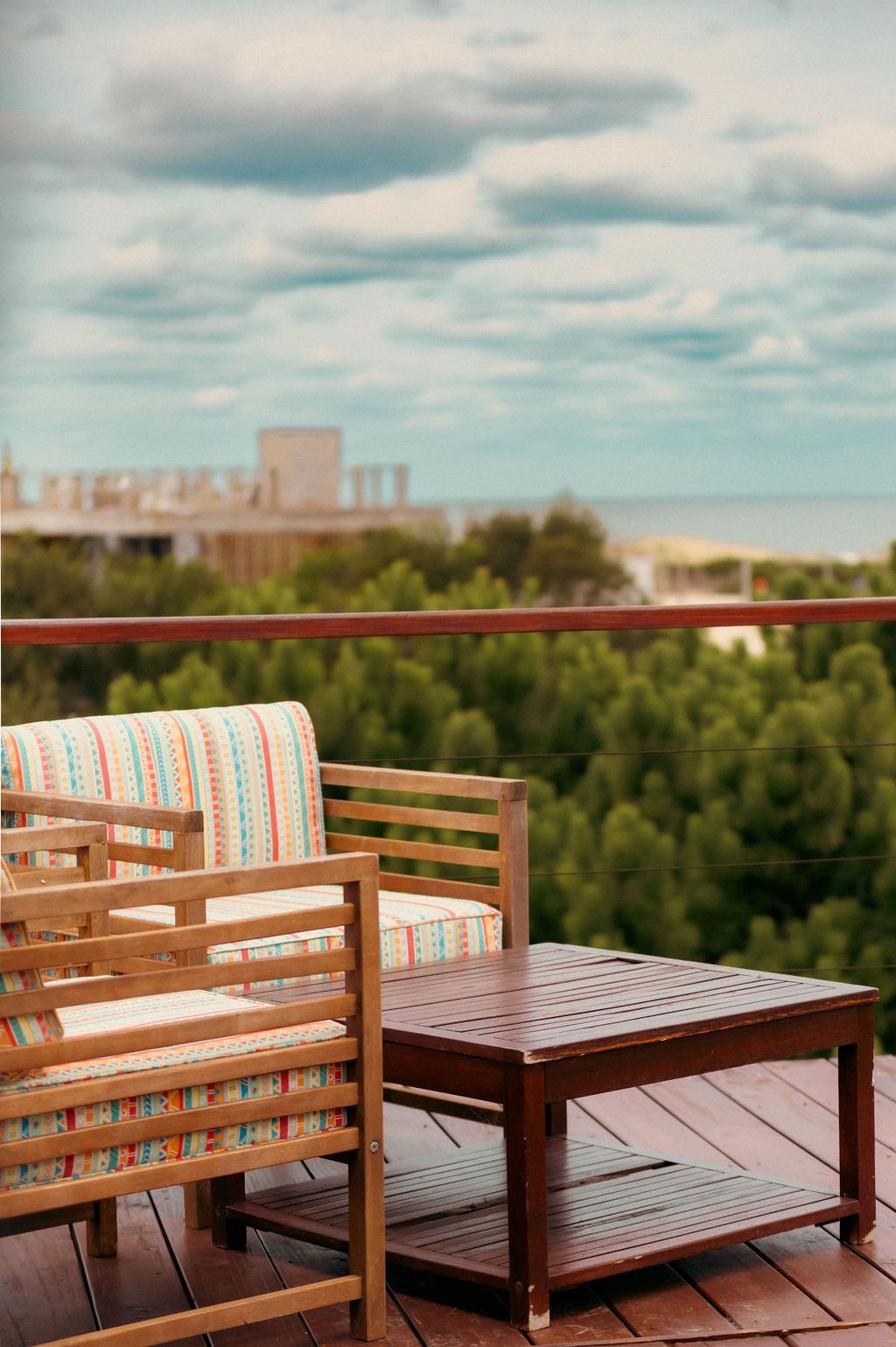 Mobiliario de patio de madera en una terraza con vista al océano y árboles bajo un cielo nublado.