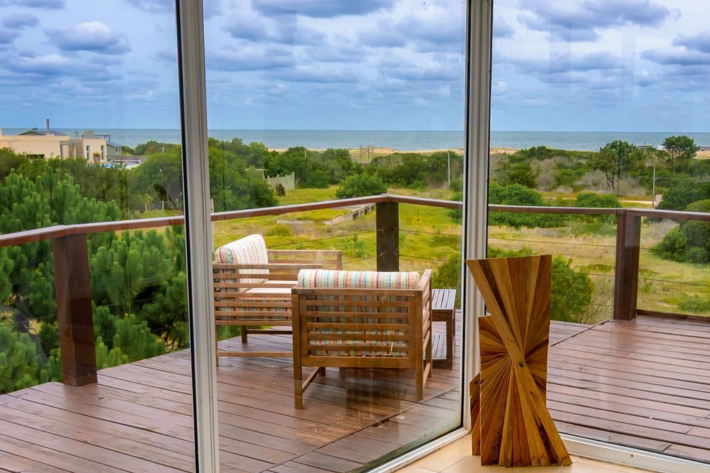 Terraza de madera con asientos con vista a las dunas y al océano a través de puertas de vidrio.