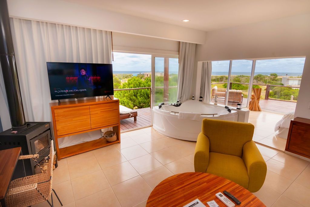 Sala con vista al mar, jacuzzi, TV en mueble de madera, sillón amarillo, mesa redonda.