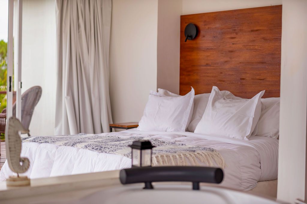 Dormitorio con cama, ropa de cama blanca, cabecero de madera, ventana, cortinas y un caballito de mar decorativo.