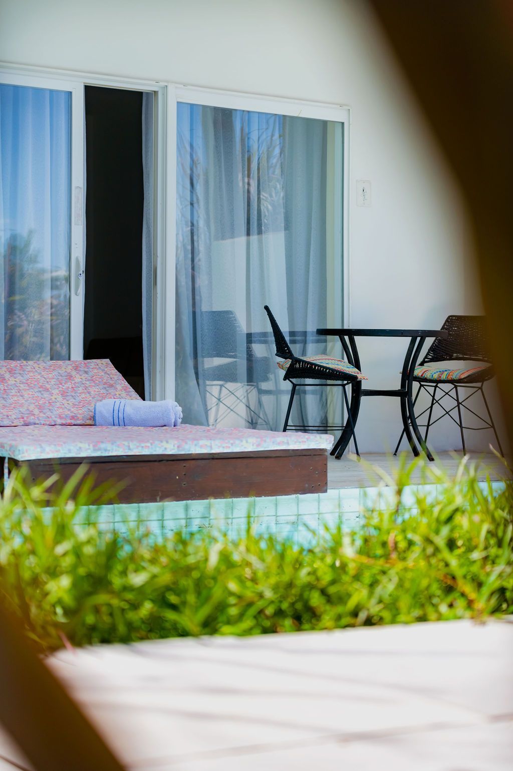 Patio con reposera, mesa y sillas junto a puertas corredizas, cerca de césped y piscina.