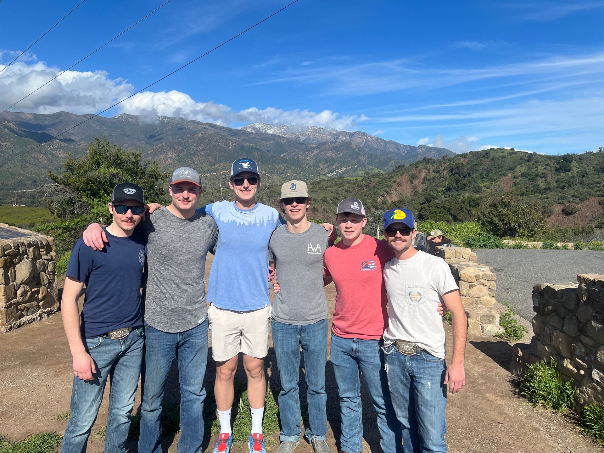 Six brothers standing with arms around each other with a mountain view behind them