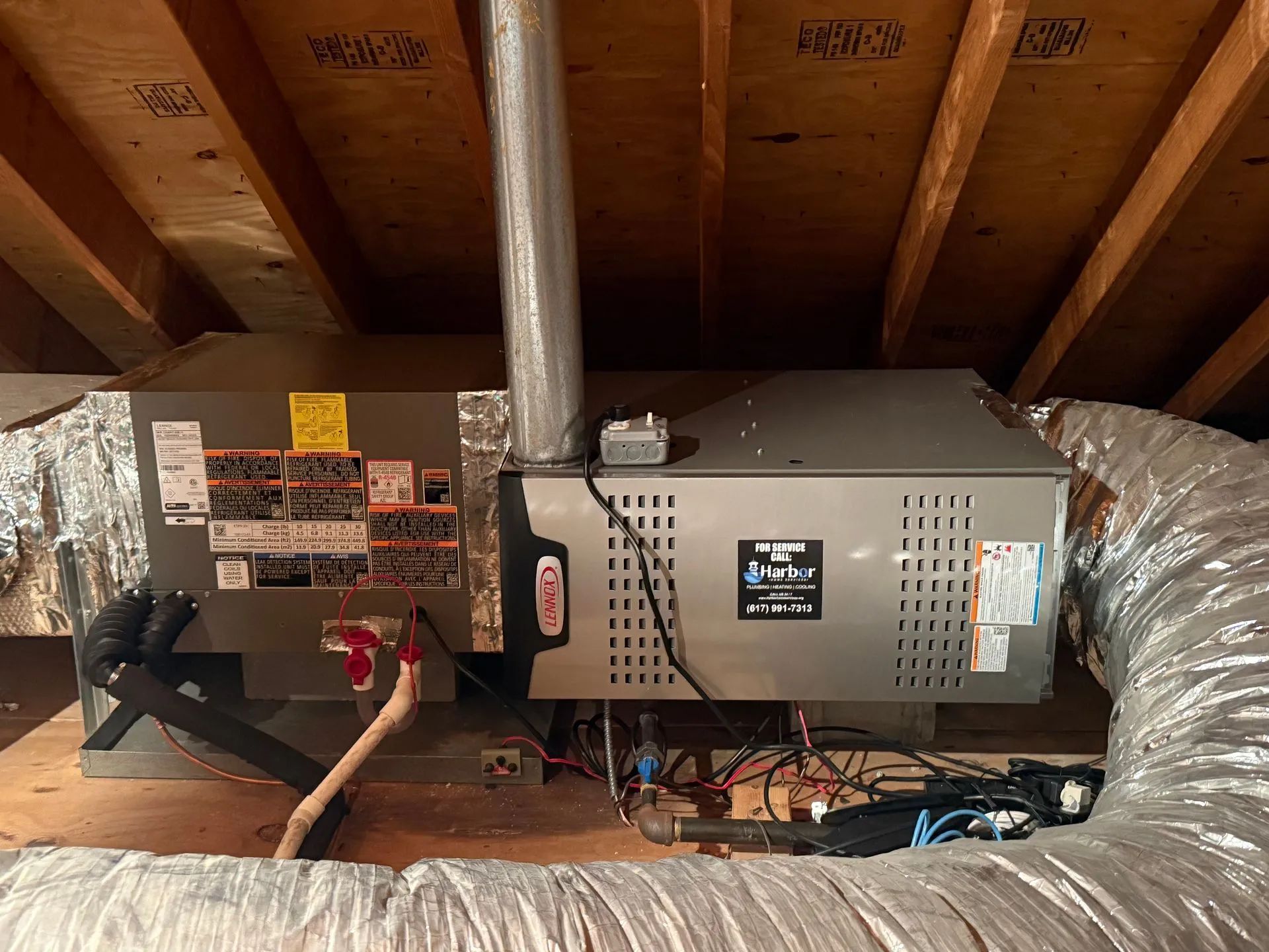 Attic HVAC furnace and water heater with silver ductwork and exposed wooden rafters