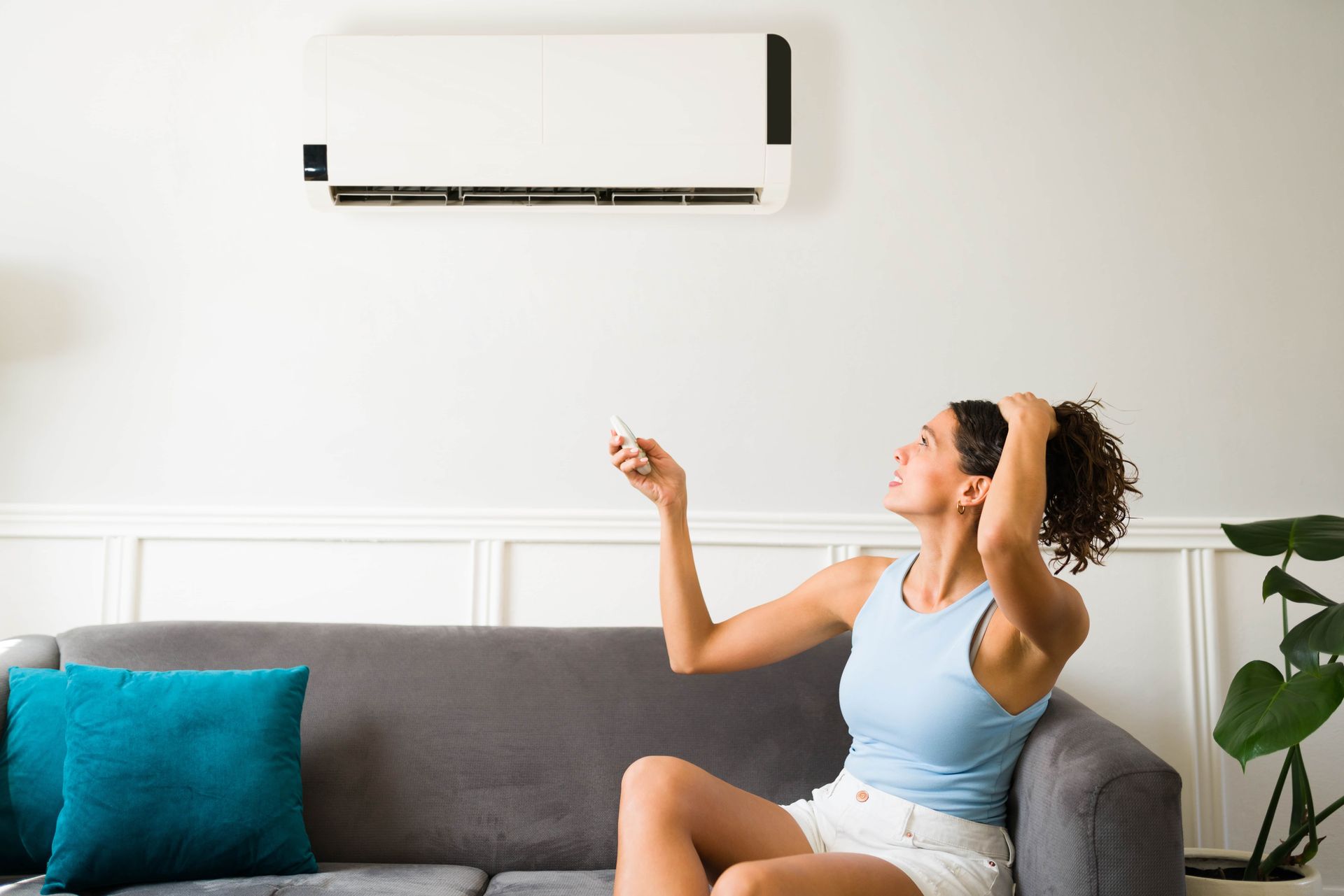 Woman stretching on a sofa in a bright living room under a wall-mounted air conditioner