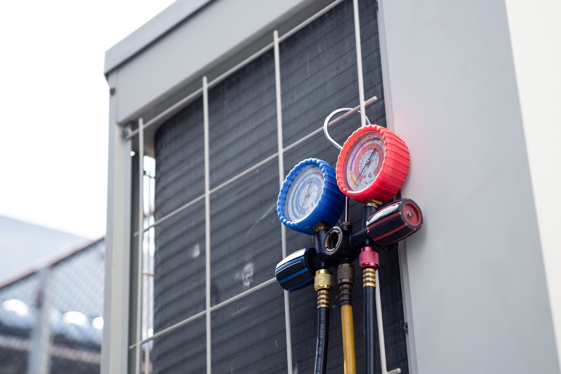 Two gauges, blue and red, hanging on pipes beside a window air conditioner unit