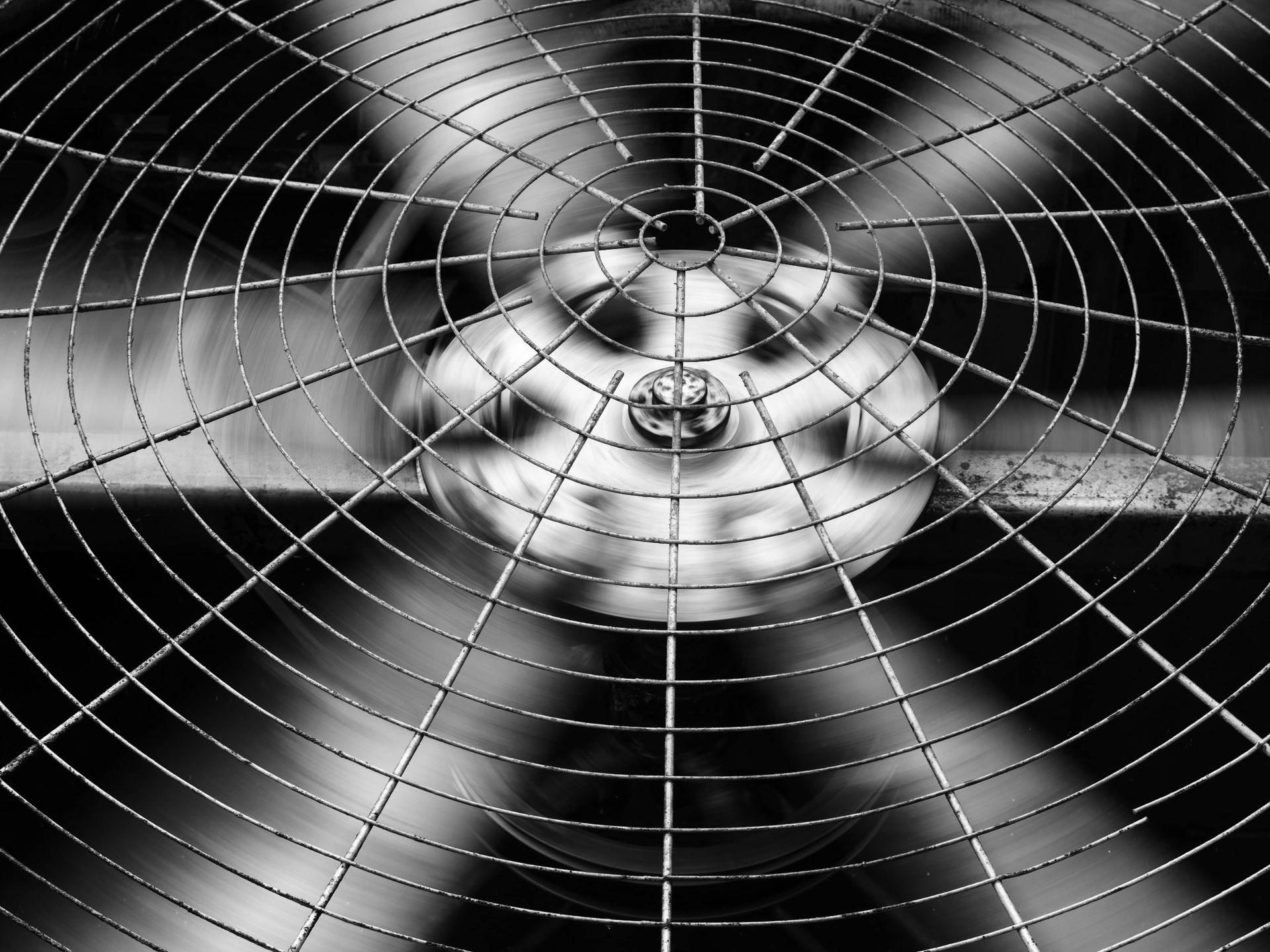 Close-up of a metal fan behind a wire safety grille, viewed from the front