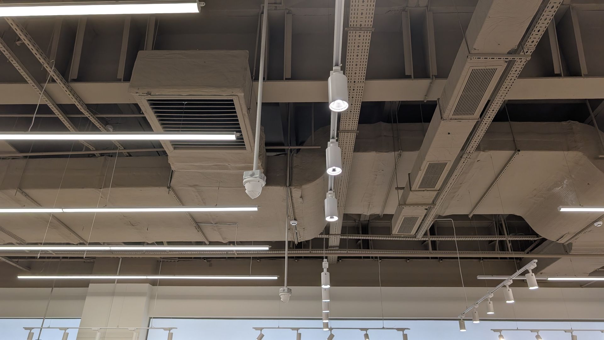 Ceiling with exposed ductwork, pipes, and rows of fluorescent lights in an industrial-style interior