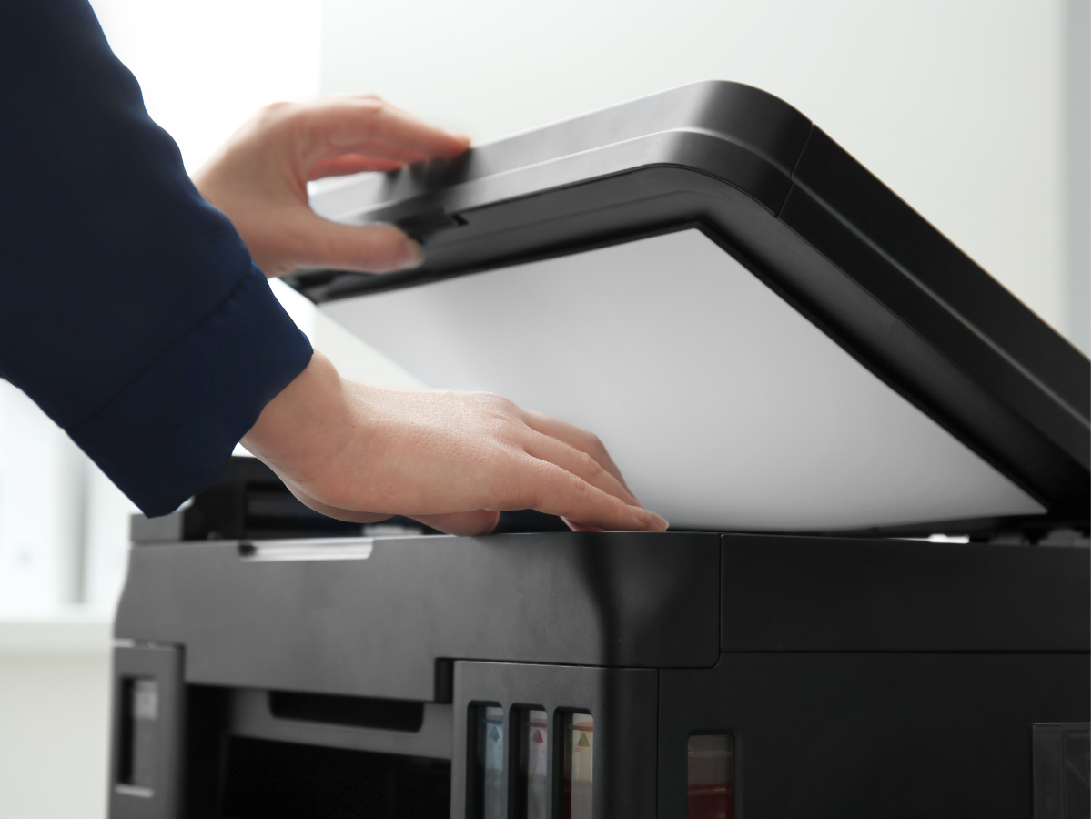 Hands opening the lid of a black multifunction printer