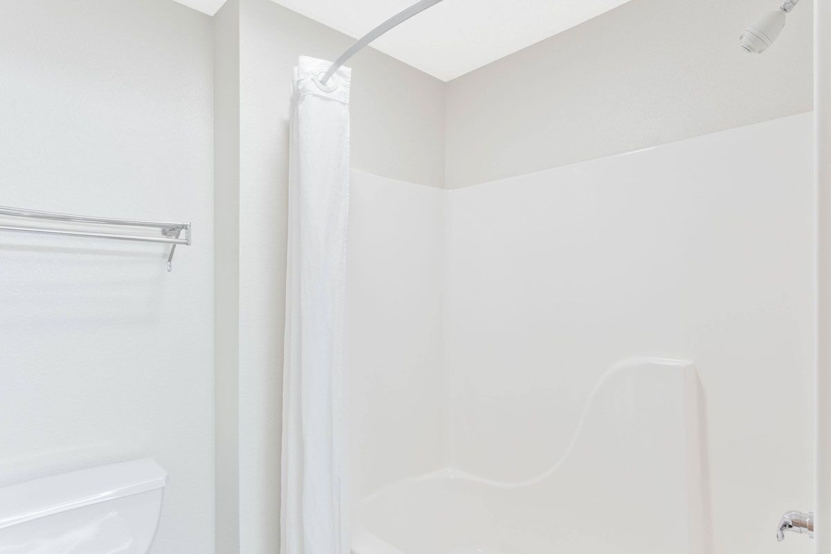 A bright, clean bathroom featuring a white bathtub and shower with a curved curtain rod and a white curtain.
