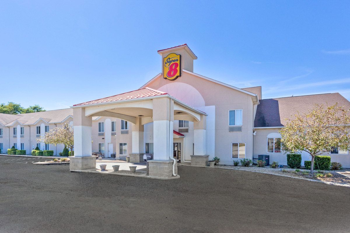 A beige Super 8 hotel building under a clear blue sky, featuring a covered entrance with pillars and sparse landscaping.