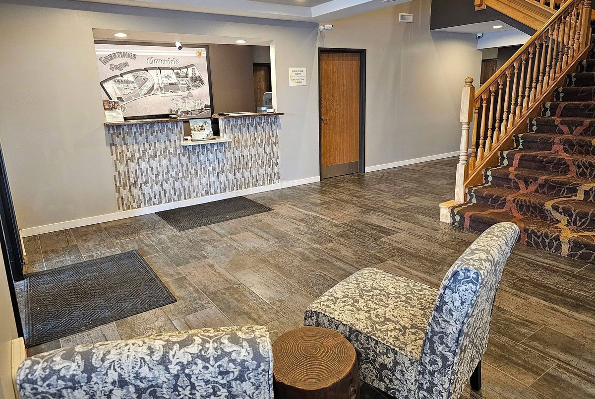 Hotel lobby featuring a reception desk with a welcome sign, patterned chairs, and a staircase.