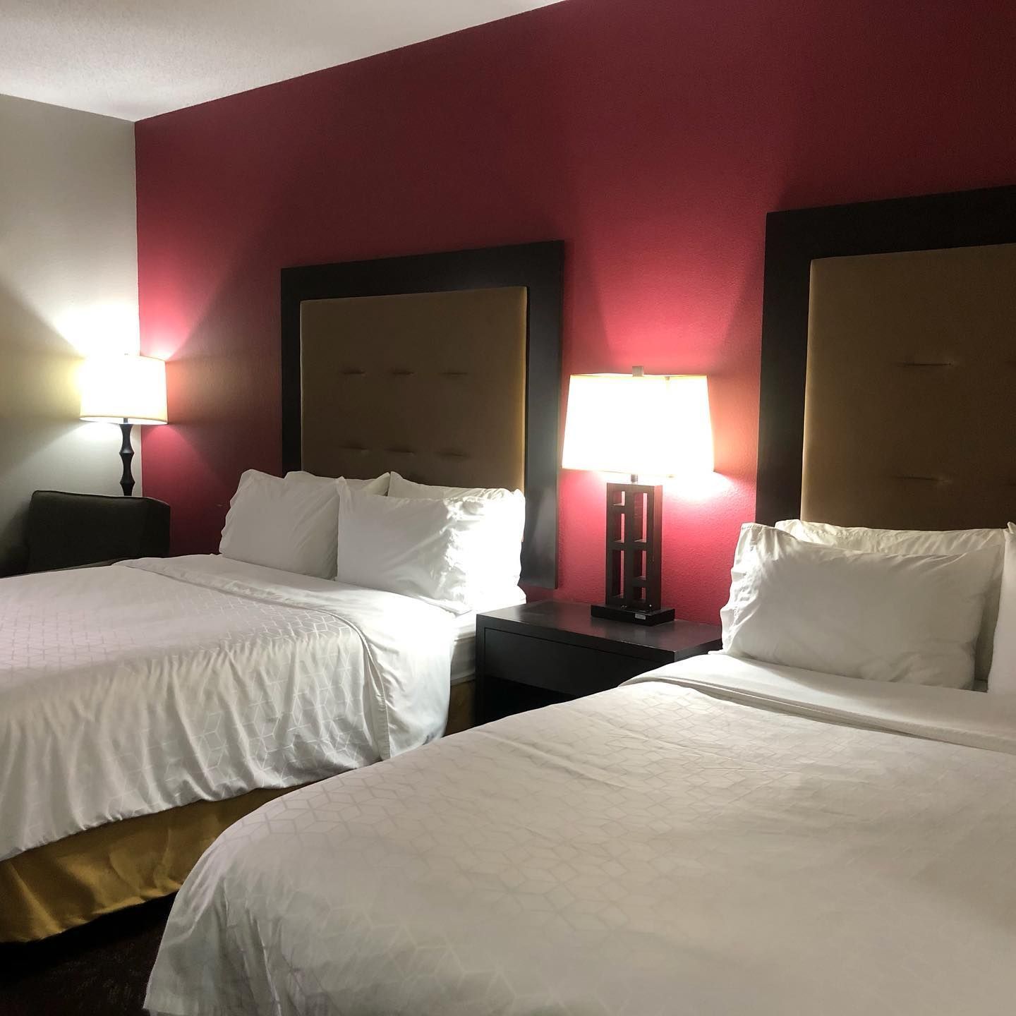 Two beds with white linens and gold bed skirts sit against a deep magenta wall with matching brown headboards and lamps.