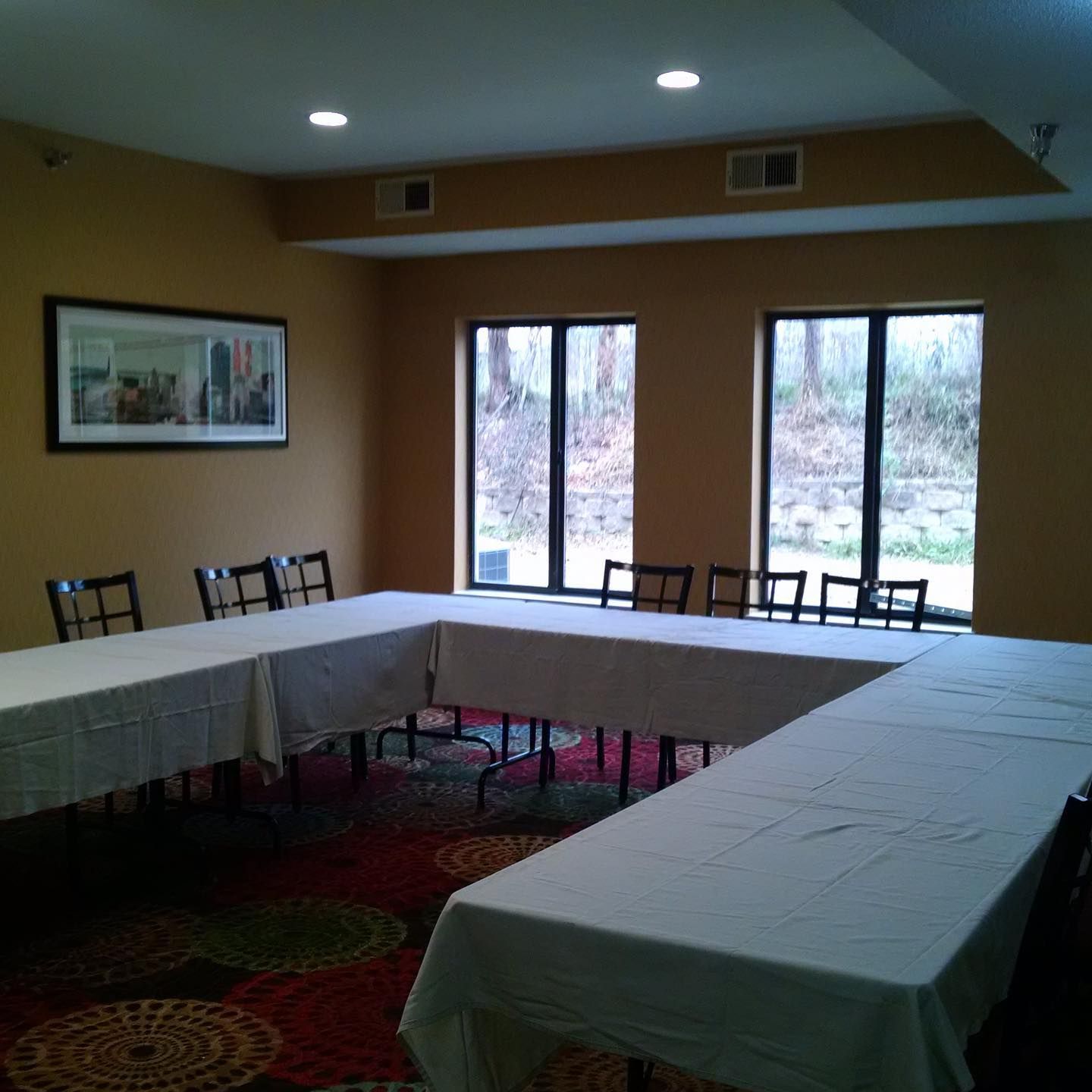 A U-shaped configuration of tables with white cloths in a meeting room with beige walls and a patterned carpet.