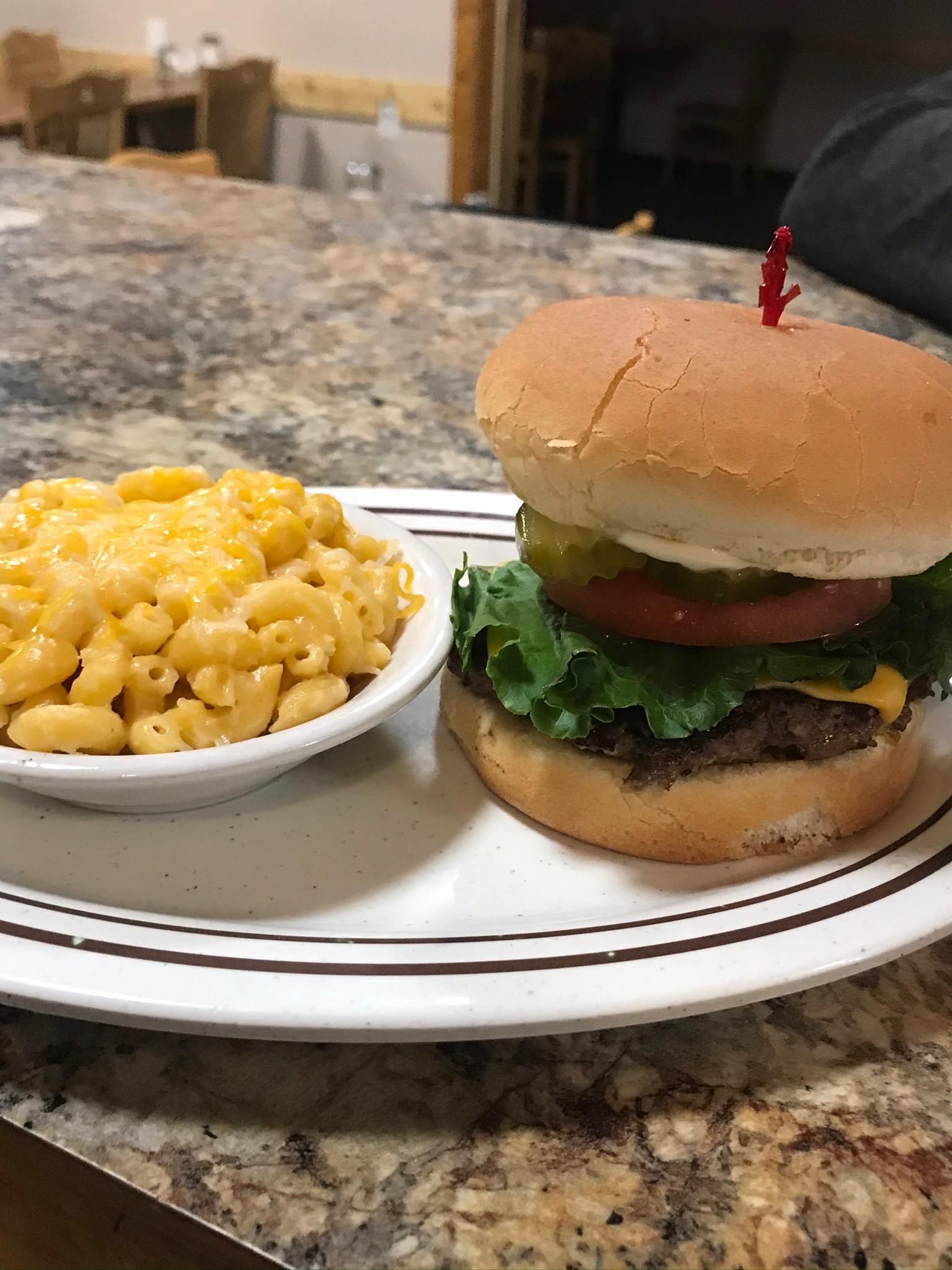 A cheeseburger with lettuce and tomato next to a bowl of macaroni and cheese on a white plate with brown stripes.