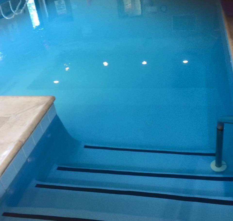 A swimming pool interior view showing shallow steps with black safety strips descending into vibrant blue water.