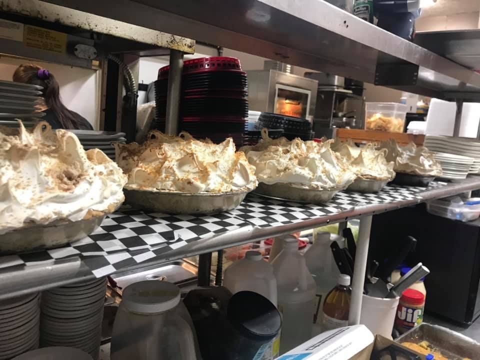 Several freshly baked meringue pies lined up on a checkered shelf in a commercial kitchen.