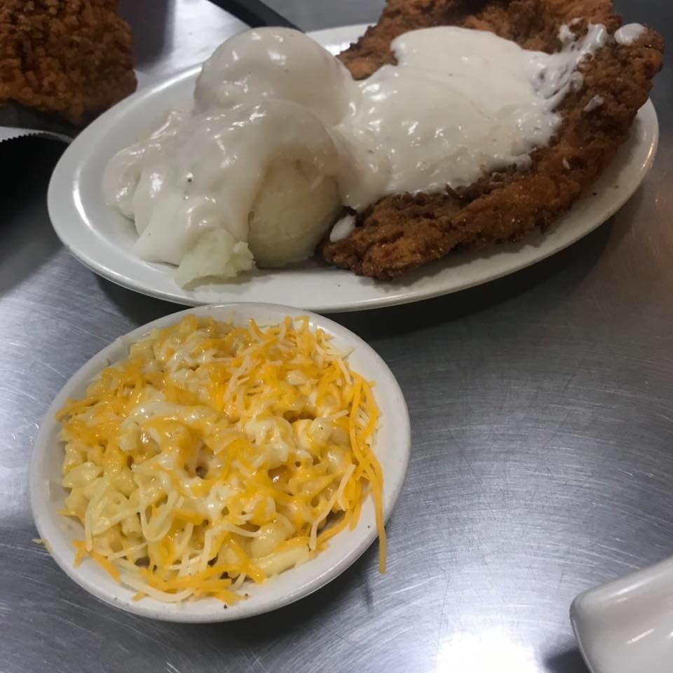 A plate of chicken fried steak with mashed potatoes and white gravy, served with a side dish of macaroni and cheese.