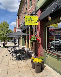 Sidewalk cafe with black tables, yellow sign, brick storefront, and flower pots on a sunny street.