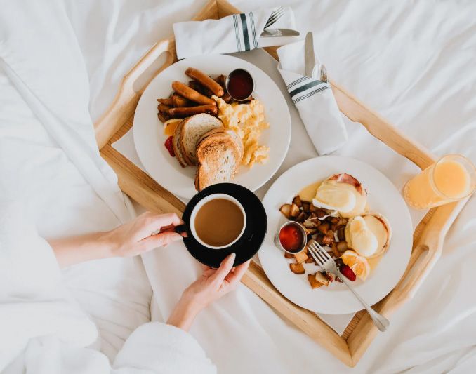 Breakfast in bed on a wooden tray: eggs, toast, sausage, coffee, orange juice, and eggs benedict.
