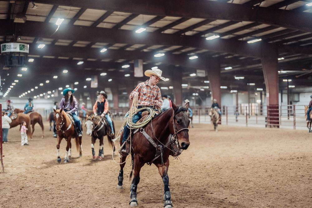 People riding horses in an indoor arena, likely at a rodeo competition.