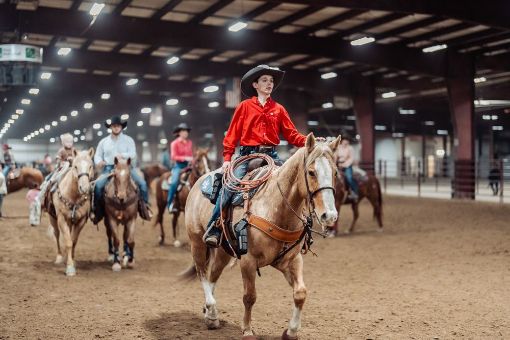 People on horseback in an indoor arena, the focus on a person in red shirt riding a palomino horse.