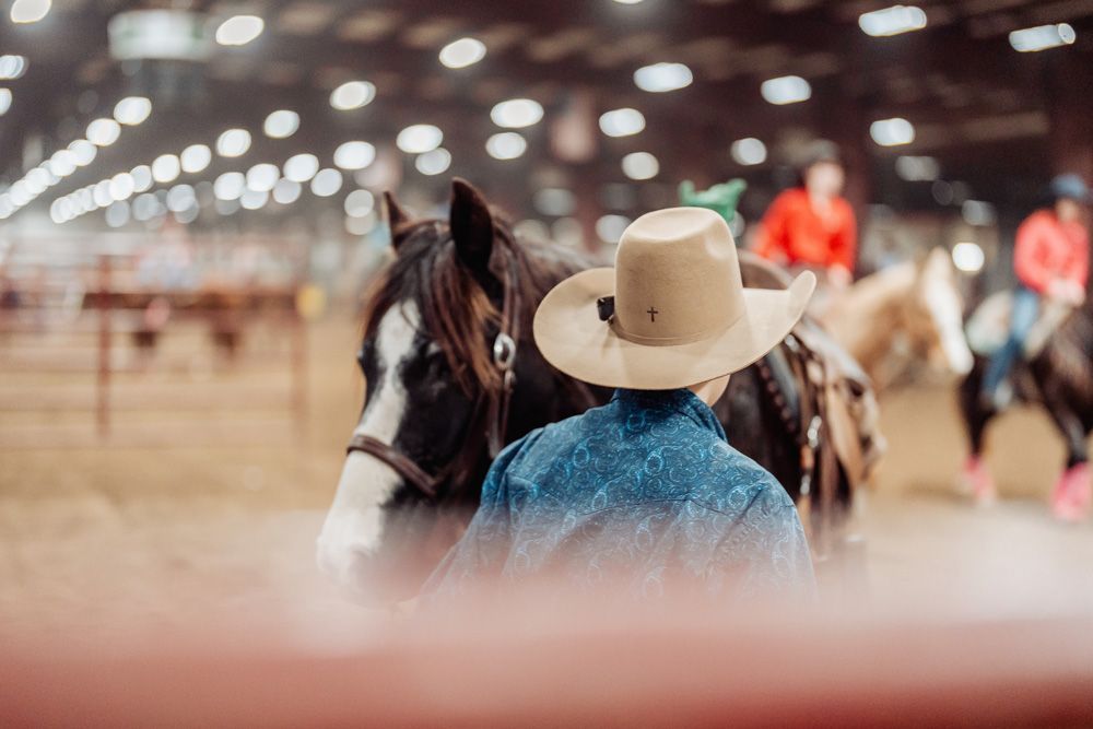 Cowboy with tan hat and horse in an indoor arena, other riders in the background.