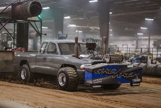 Gray pickup truck with blue front bumper driving through a muddy indoor off-road arena