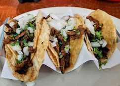 Three tacos filled with meat, onions, and cilantro on a white plate